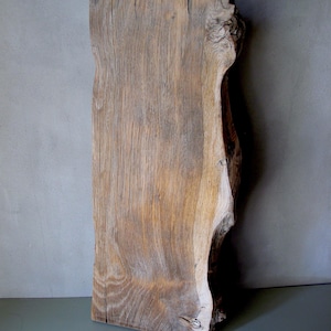 Pode incluir: Uma laje de madeira retangular e envelhecida, com uma borda natural e irregular. O veio da madeira é visível, mostrando tons de castanho e bege. A laje tem cerca de 76 cm de comprimento.