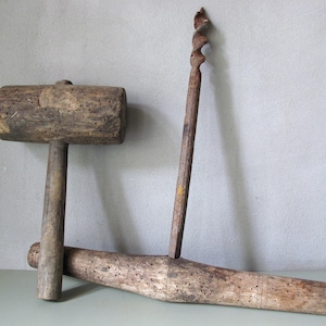 Könnte beinhalten: Ein Set antiker Holzwerkzeuge, darunter ein Hammer, ein Bohrer und ein Reibahle. Der Hammer hat einen zylindrischen Kopf und einen Griff. Der Bohrer hat einen Spiralbohrer, und die Reibahle ist ein langes, konisches Holzwerkzeug. Alle Werkzeuge weisen Alters- und Gebrauchsspuren auf.