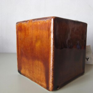 May include: A square, ceramic planter with a glossy, brown glaze. The cube-shaped pot has a rich, warm color gradient, transitioning from lighter shades at the top to darker tones at the base. The planter is suitable for indoor or outdoor use.