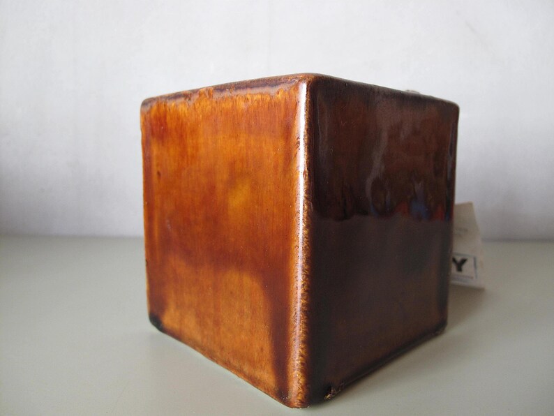 May include: A square, ceramic planter with a glossy, brown glaze. The cube-shaped pot has a rich, warm color gradient, transitioning from lighter shades at the top to darker tones at the base. The planter is suitable for indoor or outdoor use.