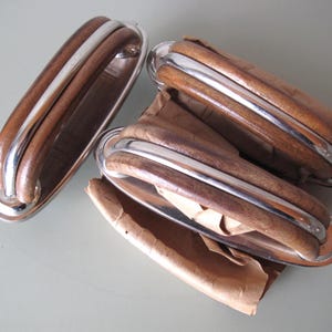 Może przedstawiać: Zestaw uchwytów do szafek w stylu vintage, wykonanych z drewna i chromu. Uchwyty mają zakrzywiony kształt z polerowanym chromowanym akcentem i bogatym brązowym usłojeniem drewna. Uchwyty są prostokątne i wydają się nowe, niektóre w oryginalnym opakowaniu.