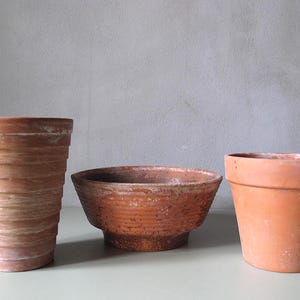 Può includere: Tre vasi di terracotta di varie forme e dimensioni. Il vaso più alto è cilindrico con creste orizzontali. Il vaso centrale ha la forma di una ciotola bassa. Il terzo vaso ha una forma classica, leggermente conica.