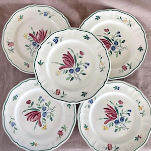 May include: A set of five off-white ceramic plates with scalloped edges and a dark green rim. Each plate features a central hand-painted floral motif with a large maroon flower, small blue berries, and green leaves, accented by smaller floral sprigs.
