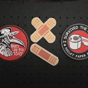 Könnte beinhalten: Gestickte Aufnäher mit humorvollen Themen. Ein Aufnäher zeigt einen Pestdoktor mit dem Text "Party Like It's 1349". Ein anderer sagt "I Survived The Great Toilet Paper Crisis 2020". Zwei Pflaster-Aufnäher sind ebenfalls enthalten.