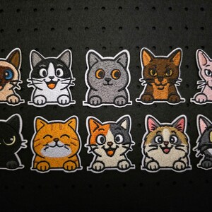 Könnte beinhalten: Zehn gestickte Katzenaufnäher in verschiedenen Farben und Designs. Jeder Aufnäher zeigt eine andere Katze mit einzigartigen Gesichtsausdrücken und Markierungen. Die Katzen sind weiß umrandet.