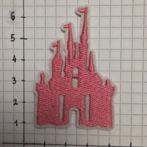 Op de afbeelding: Roze geborduurde kasteelpatch met een witte rand. Het kasteel heeft meerdere torentjes en ramen. De patch is ongeveer 5 cm breed en 7,5 cm hoog.