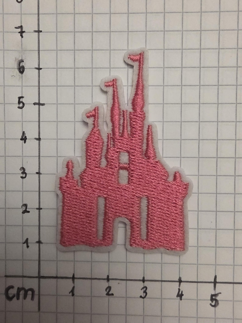 Op de afbeelding: Roze geborduurde kasteelpatch met een witte rand. Het kasteel heeft meerdere torentjes en ramen. De patch is ongeveer 5 cm breed en 7,5 cm hoog.