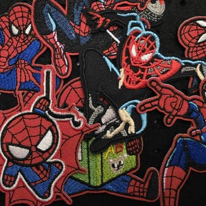 Könnte beinhalten: Eine Sammlung von aufgestickten Aufnähern mit dem Superhelden Spider-Man in verschiedenen Actionposen. Die Aufnäher zeigen das ikonische rot-blaue Kostüm der Figur mit weißen Augen und Spinnennetz-Designs. Einige Aufnäher sind im Cartoon-Stil gehalten.