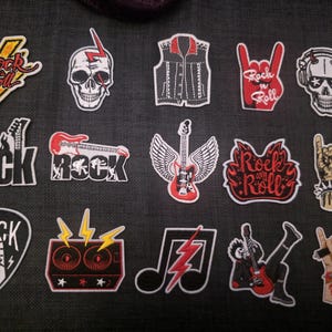 Könnte beinhalten: Eine Sammlung von Rock'n'Roll-Patches. Designs umfassen Totenköpfe, Gitarren, Blitze und die Wörter "Rock" und "Rock and Roll". Die Patches sind in verschiedenen Farben gehalten, darunter Rot, Schwarz, Weiß und Gelb.