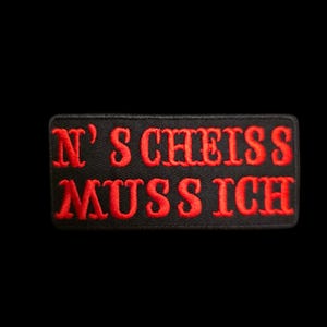 Könnte beinhalten: Ein rechteckiger, schwarz bestickter Aufnäher mit dem in Rot gestickten Text N' S CHEISS MUSS ICH in zwei Zeilen. Der Aufnäher hat einen sauber verarbeiteten Rand und ist zur Befestigung auf Textilien durch Nähen oder Aufbügeln vorgesehen.