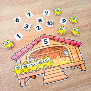Pode incluir: Um conjunto educativo de contagem com um grande galinheiro ilustrado com telhado vermelho e cinco pintinhos amarelos, acompanhado por dez cartões quadrados numerados de um a dez e quatro recortes individuais de pintinhos amarelos.