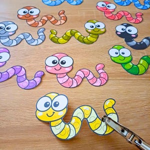 Puede incluir: Una colección de recortes de gusanos de dibujos animados coloridos en varios tonos incluyendo amarillo, rosa, verde, azul, naranja y gris, cada uno con grandes ojos blancos y una cara sonriente, con una perforadora de metal en el gusano amarillo.