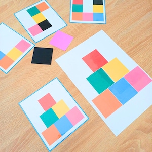 Könnte beinhalten: Eine Sammlung weißer Karten mit bunten Quadratmustern in Rot, Gelb, Grün, Blau, Orange, Pink und Schwarz. Das Set enthält lose quadratische Papierstücke in Pink und Schwarz, die in verschiedenen geometrischen Mustern angeordnet sind.