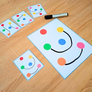 May include: A set of four white rectangular cards featuring colorful dots connected by black lines, accompanied by a black marker. The cards display various patterns of red, yellow, blue, green, orange, and pink circles linked by straight, curved, or zigzag lines.
