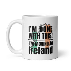 Puede incluir: Taza de cerámica blanca con el texto "I'M DONE WITH THIS! I'M MOVING TO Ireland" en negro. El diseño incluye un mapa de Irlanda con acentos verdes y naranjas, representando la bandera irlandesa.