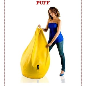 May include: A large, yellow beanbag chair. The beanbag is teardrop-shaped and appears to be made of a smooth fabric. The text "FABRICA TU PROPIO PUFF" is displayed in red at the top of the image.