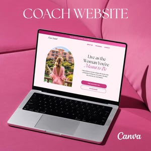 May include: A silver laptop displaying a website with the text "Coach Website" and "Live as the Woman You're Meant to Be." The laptop is on a pink surface. The website features a woman in a pink dress.