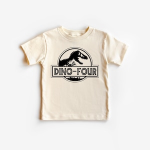 May include: Cream-colored short-sleeved t-shirt with a black dinosaur graphic inside a circular emblem. The text "DINO-FOUR" is printed in a rectangular box below the emblem. The shirt is designed for a child's fourth birthday.
