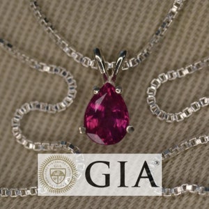 May include: A pear-shaped pink gemstone pendant on a silver chain. The pendant is set in a silver setting and has a GIA certification.