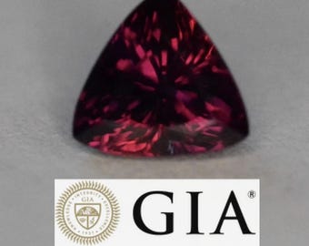 May include: A triangular, faceted gemstone with a deep red hue. The gem has a complex internal structure, reflecting light. The GIA logo is visible below the gemstone, indicating its certification.