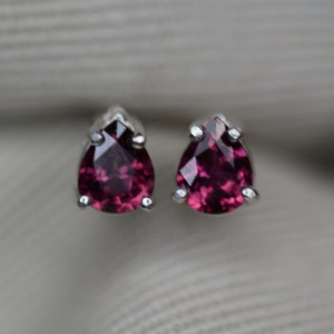 May include: A pair of sterling silver stud earrings with pear-shaped, deep pink gemstones.