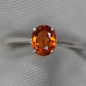 May include: A silver ring with an oval-shaped orange gemstone set in a prong setting.