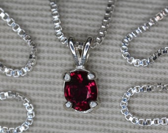 May include: A silver chain necklace with a pendant featuring a red oval gemstone.