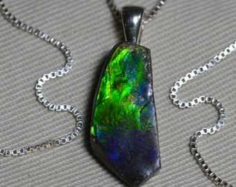 May include: A silver chain necklace with a pendant featuring a large, iridescent green and black gemstone. The gemstone has a rough, natural shape and is set in a silver bezel.