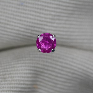 May include: A vibrant pink gemstone set in a silver prong setting. The gemstone is round and has a smooth, polished surface.