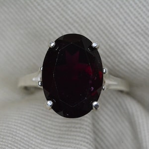 May include: A silver ring with a large, oval-shaped, dark red gemstone.