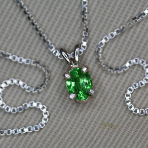 May include: A silver chain necklace with a pendant featuring a green oval gemstone.
