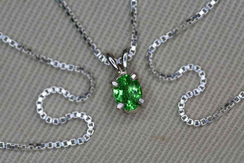 May include: A silver chain necklace with a pendant featuring a green oval gemstone.