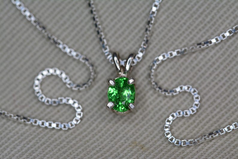 May include: A silver chain necklace with a green oval gemstone pendant.