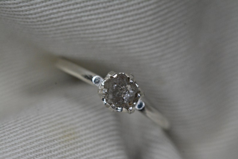 May include: A silver ring with a rough, gray diamond set in a prong setting.