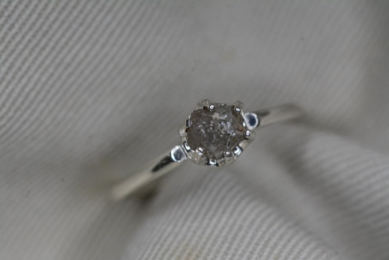 May include: A silver ring with a rough, gray diamond set in a prong setting.