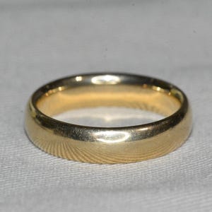May include: A simple gold wedding band with a smooth, rounded surface.