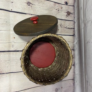 May include: A woven wicker basket with a red liner and a wooden lid with a red knob.