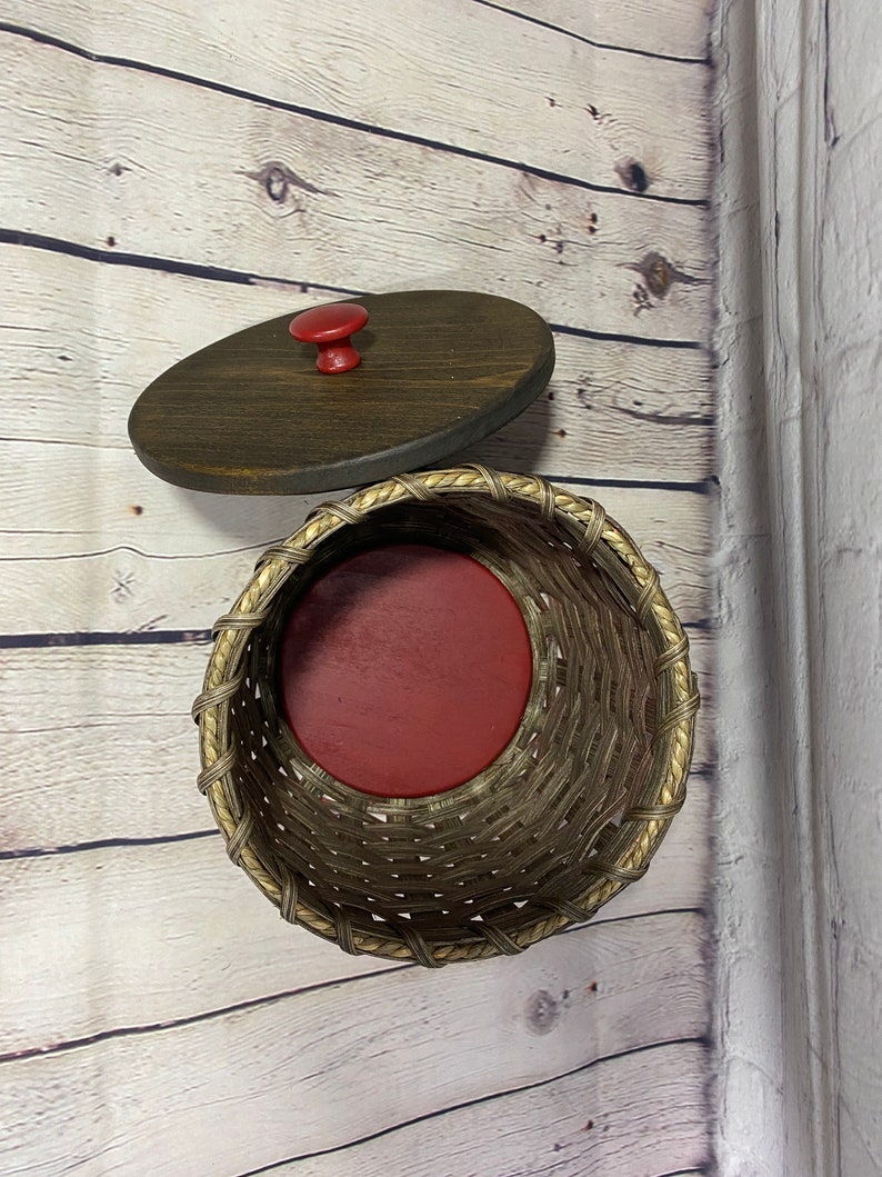 May include: A woven wicker basket with a red liner and a wooden lid with a red knob.