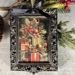 May include: A black framed ornament with a vintage Christmas image of presents, holly, and ornaments. The frame has a gold-like finish and ornate details.