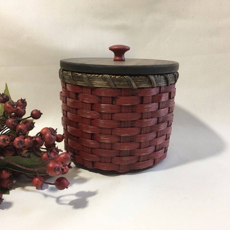 May include: A red woven basket with a wooden lid and knob. The lid has a dark brown wood finish and a gold trim.