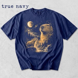 May include: True navy blue t-shirt featuring a detailed illustration of capybaras under a full moon. The design includes a large capybara with a smaller one, a waterfall, and a forest. The text "true navy" is at the top.