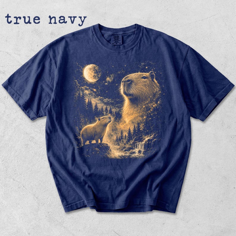 May include: True navy blue t-shirt featuring a detailed illustration of capybaras under a full moon. The design includes a large capybara with a smaller one, a waterfall, and a forest. The text "true navy" is at the top.