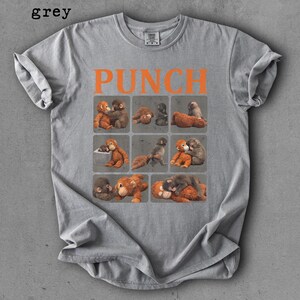 Peut inclure: T-shirt gris avec le mot "PUNCH" en lettres orange. Le t-shirt pr&eacute;sente une grille de neuf carr&eacute;s, chacun contenant une illustration diff&eacute;rente de deux singes qui s'embrassent. Le mot "grey" est dans le coin sup&eacute;rieur gauche.