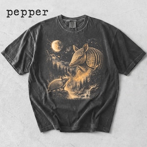 May include: Dark grey t-shirt with a detailed illustration of two armadillos in a forest scene under a full moon. The design includes a waterfall and trees, with the word "pepper" at the top.