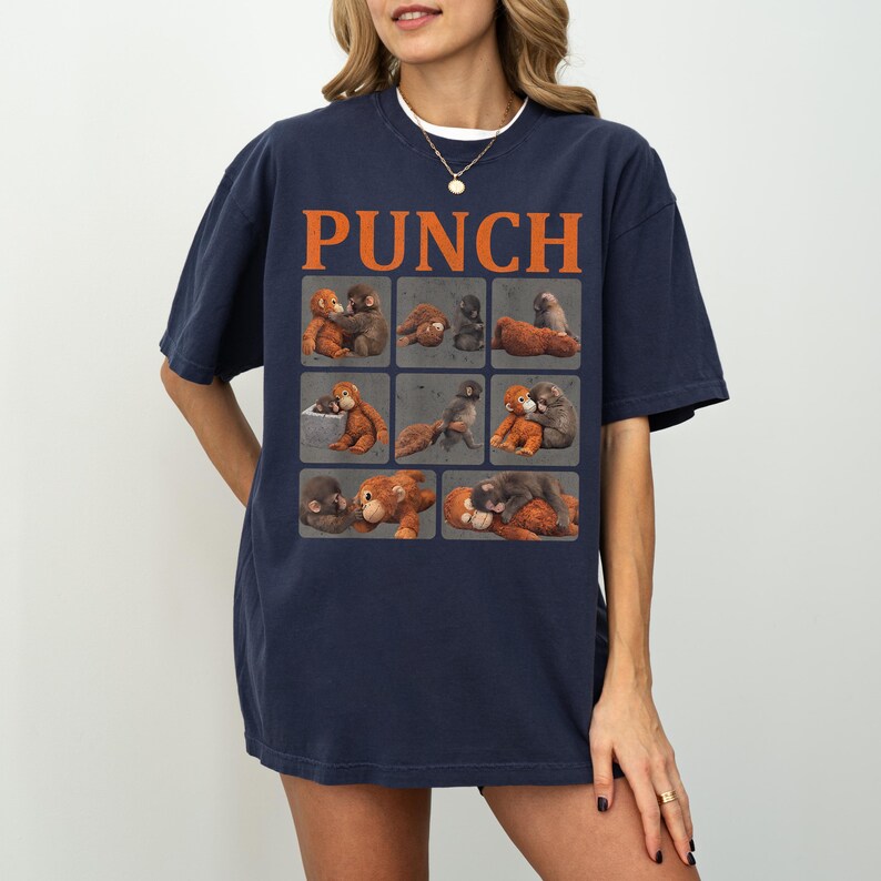 Peut inclure: T-shirt bleu marine avec le mot "PUNCH" en lettres orange. Le t-shirt pr&eacute;sente une grille de neuf carr&eacute;s, chacun contenant une illustration &agrave; l'aquarelle de singes dans diverses poses. Le t-shirt est de coupe d&eacute;contract&eacute;e.
