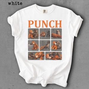 Peut inclure: T-shirt blanc avec le mot "PUNCH" en lettres orange. En dessous, neuf carr&eacute;s avec des illustrations de singes. Le t-shirt est de style col rond.