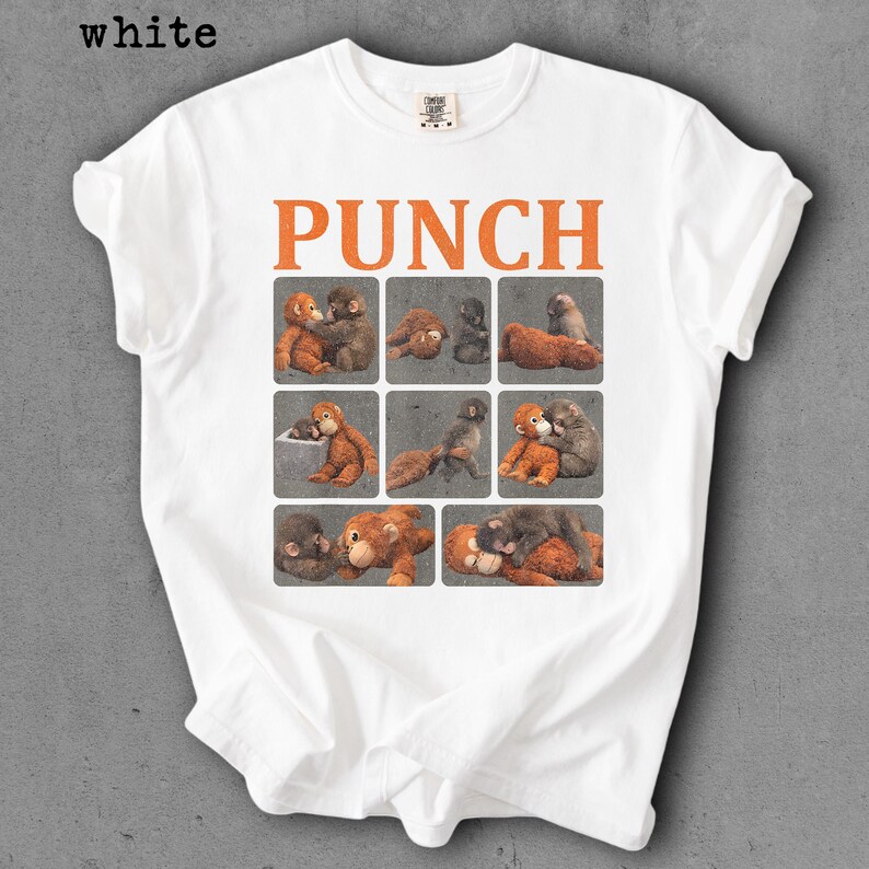 Peut inclure: T-shirt blanc avec le mot "PUNCH" en lettres orange. En dessous, neuf carr&eacute;s avec des illustrations de singes. Le t-shirt est de style col rond.