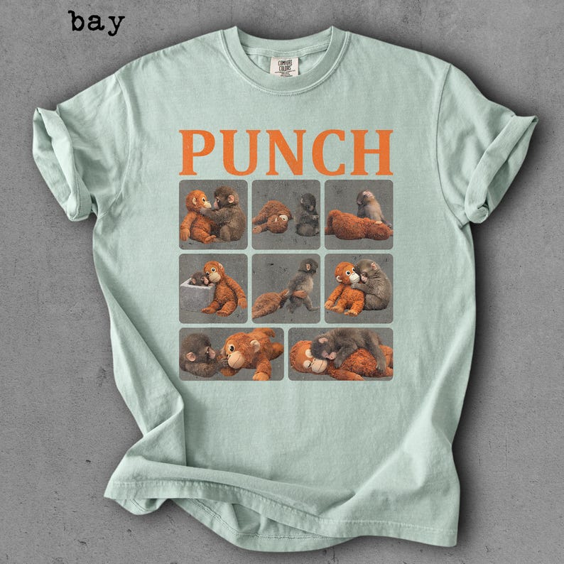 Peut inclure: T-shirt vert clair avec le mot "PUNCH" en orange. En dessous, neuf carr&eacute;s avec des illustrations de singes dans diff&eacute;rentes poses. Le t-shirt est pli&eacute;, avec les manches retrouss&eacute;es.