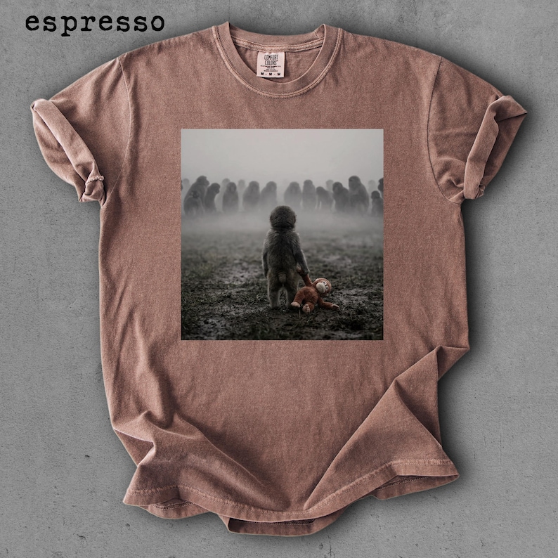 May include: Espresso-colored t-shirt featuring a square image of a child holding a teddy bear, facing a crowd in a foggy field. The shirt has a crew neck and short sleeves. The word "espresso" is printed at the top left.