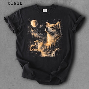 May include: Black t-shirt featuring a detailed illustration of a corgi dog looking up at the moon in a night forest scene. The word "black" is printed at the top left of the shirt.